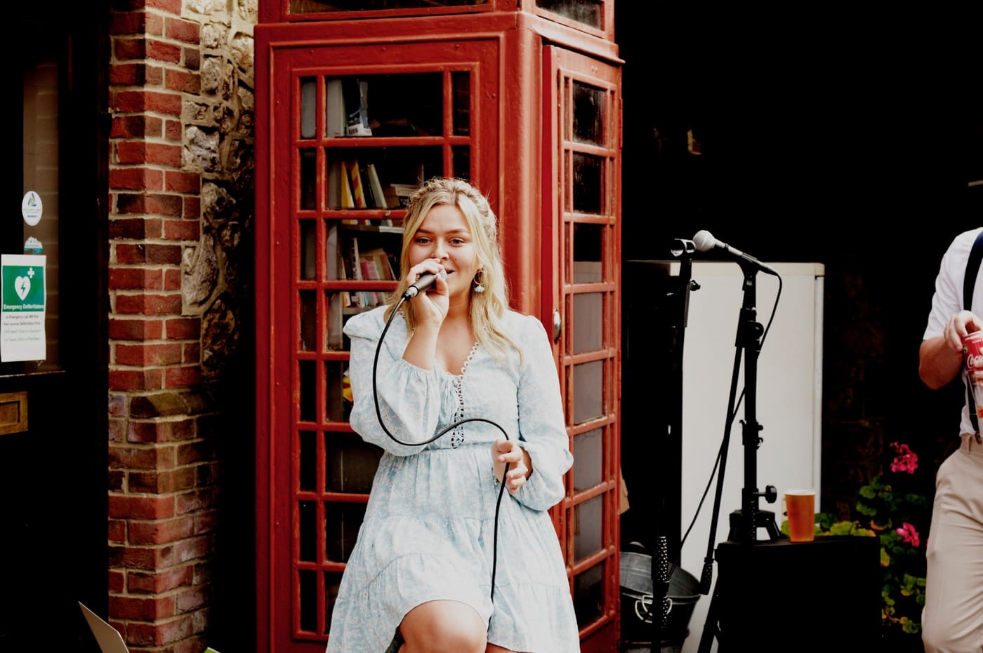 Anna singing outside a village pub beside a red telephone box