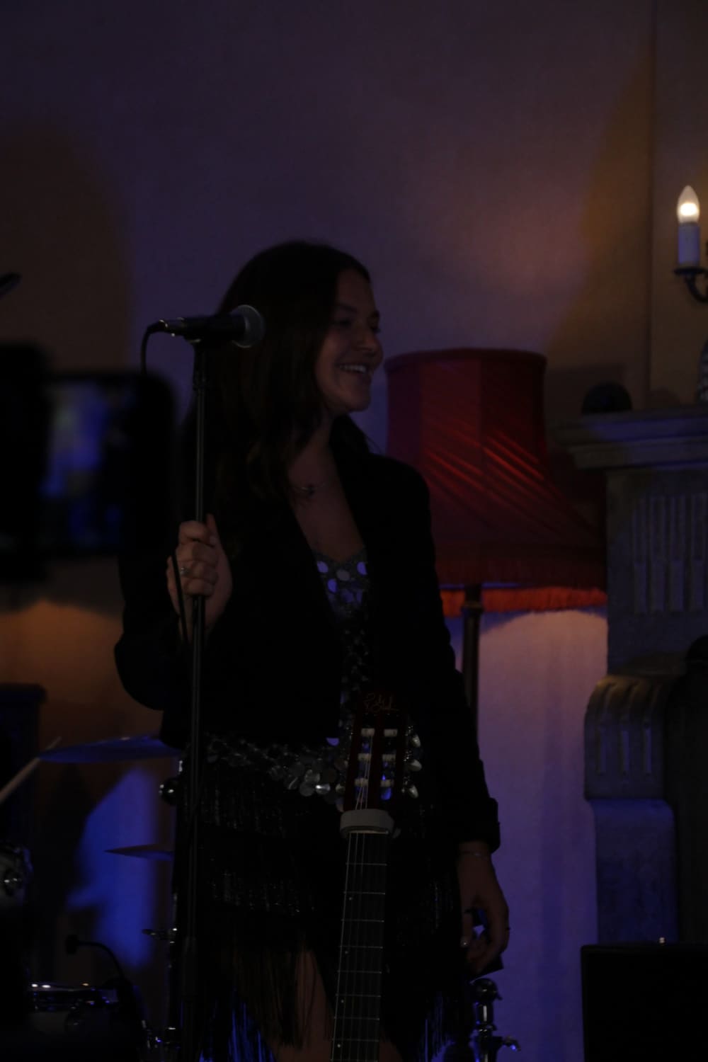 Anna on stage holding a microphone stand, guitar beside her